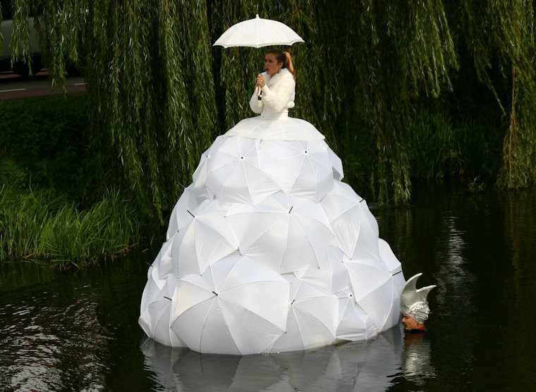 De dame in de grote witte jurk. De jurk is gemaakt van witte paraplu's.